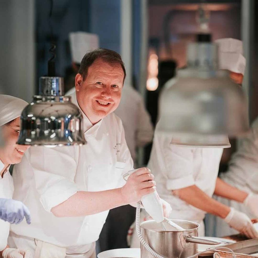 Le chef Yoann Bernard souriant en cuisine, entouré de son équipe en pleine préparation